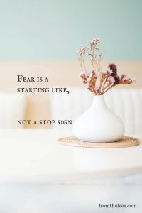 White ceramic vase holding dried flowers on a woven mat with the quote, "Fear is a starting line, not a stop sign."