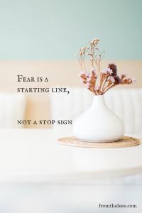White ceramic vase holding dried flowers on a woven mat with the quote, "Fear is a starting line, not a stop sign."